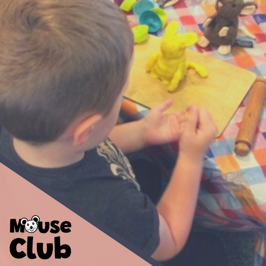 A small boy is making a model of his toy mouse out of yellow playdough.