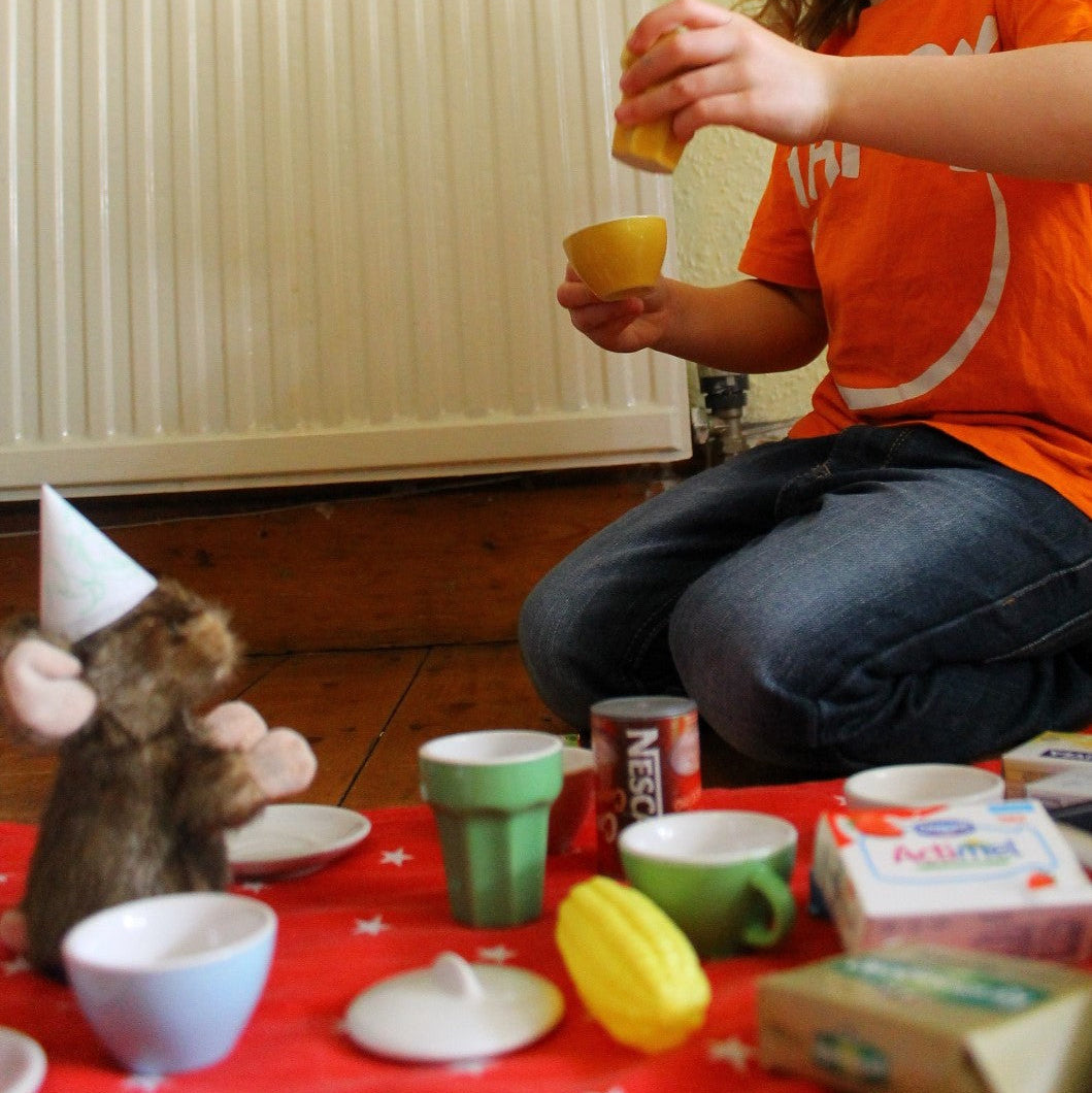 A child is sitting on the floor with a small plush mouse, playing tea party.