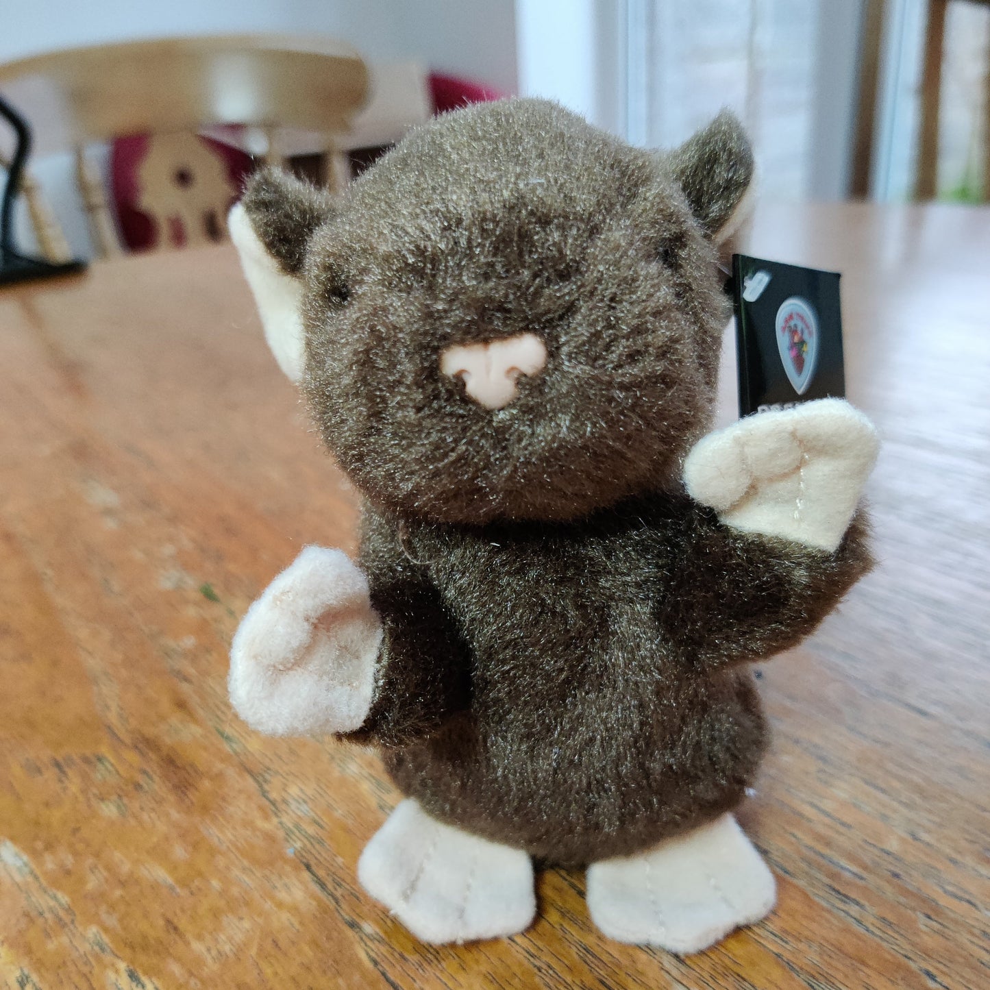 A cute brown toy mouse sits on a dining room table.