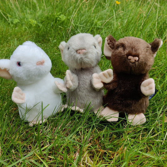 Three plush mice of different colours, white, grey and brown, are sitting on the grass. 
