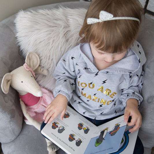 A child reads a book to her toy mouse.